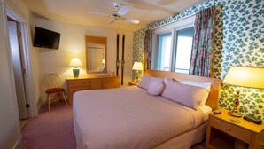 A bedroom with a large bed, two bedside tables with lamps, a wooden chair, a TV mounted on the wall, and a ceiling fan.