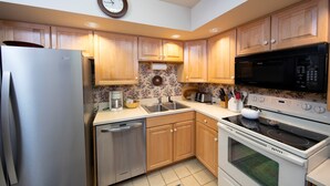 A modern kitchen with wooden cabinets, stainless steel appliances, a clock, and a floral backsplash.