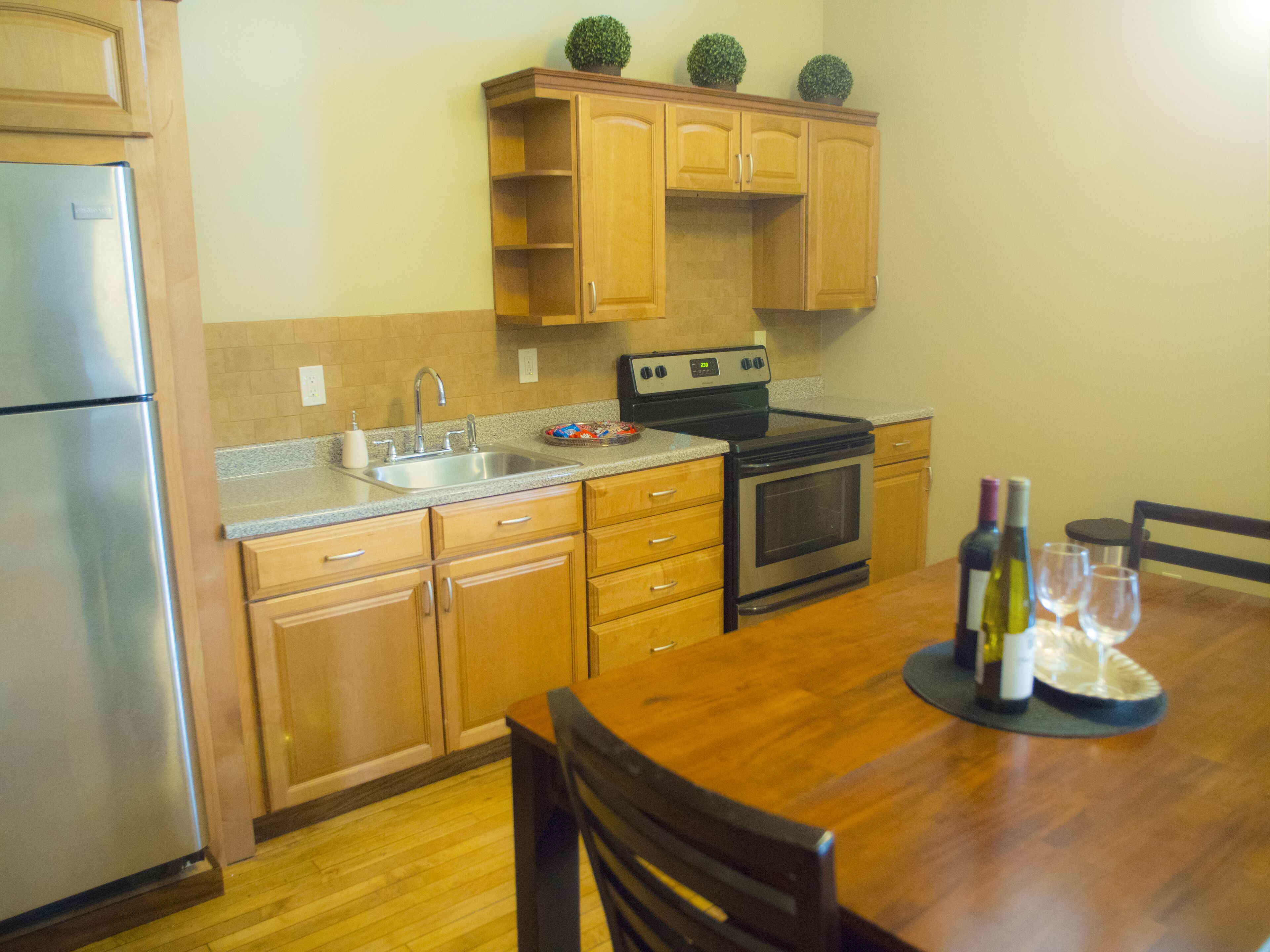 A compact kitchen with wooden cabinets, a stainless steel refrigerator, a stove, and a sink.