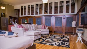 A spacious living room with a large sectional sofa, a wooden floor, and a decorative rug. - School 31 Lofts at Colors Studios (Rochester)