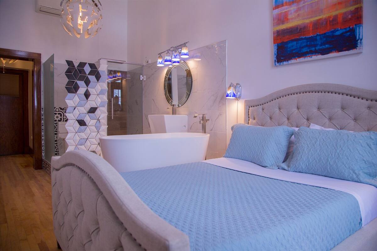 A bedroom with a large bed, a modern bathroom, and a geometric wall design.