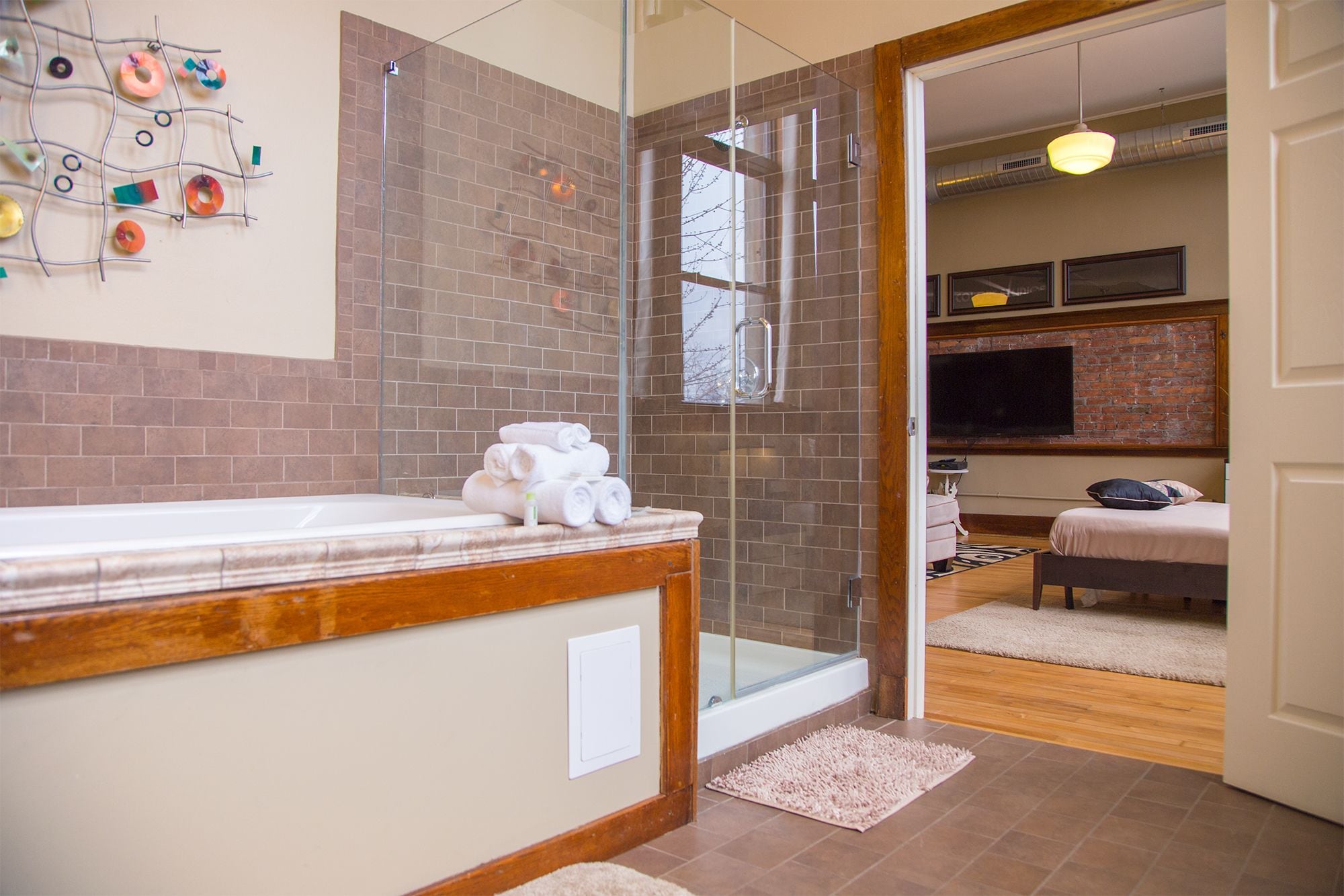 A modern bathroom with a glass shower enclosure, a wooden vanity, and a visible television in the adjacent room.