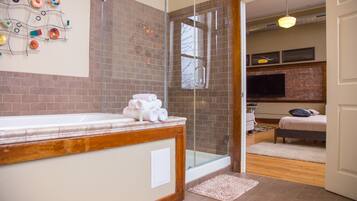 A modern bathroom with a glass shower enclosure, a wooden vanity, and a visible television in the adjacent room.