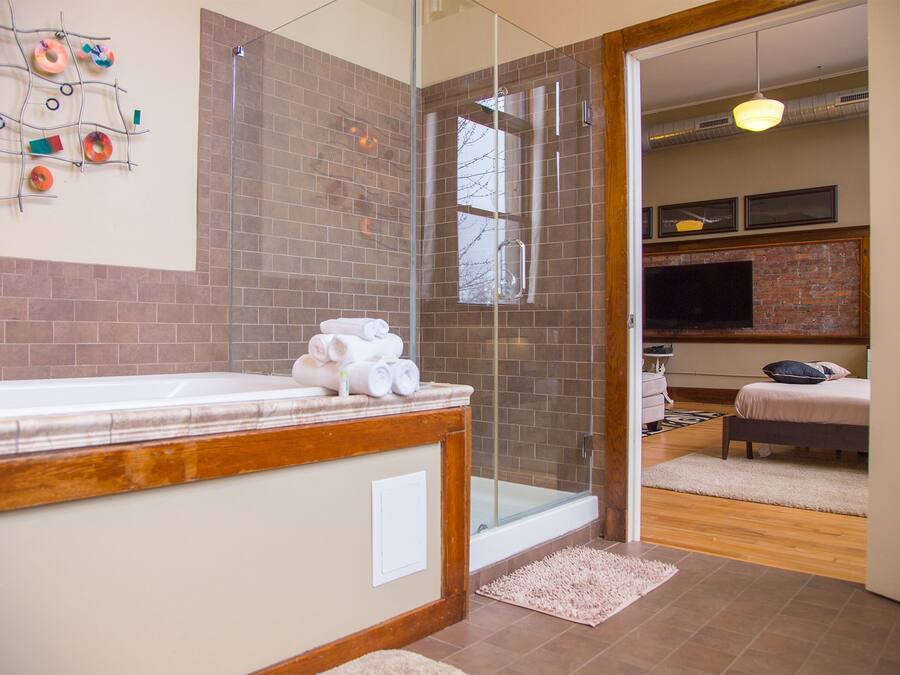 A modern bathroom with a glass shower enclosure, a wooden vanity, and a visible television in the adjacent room.