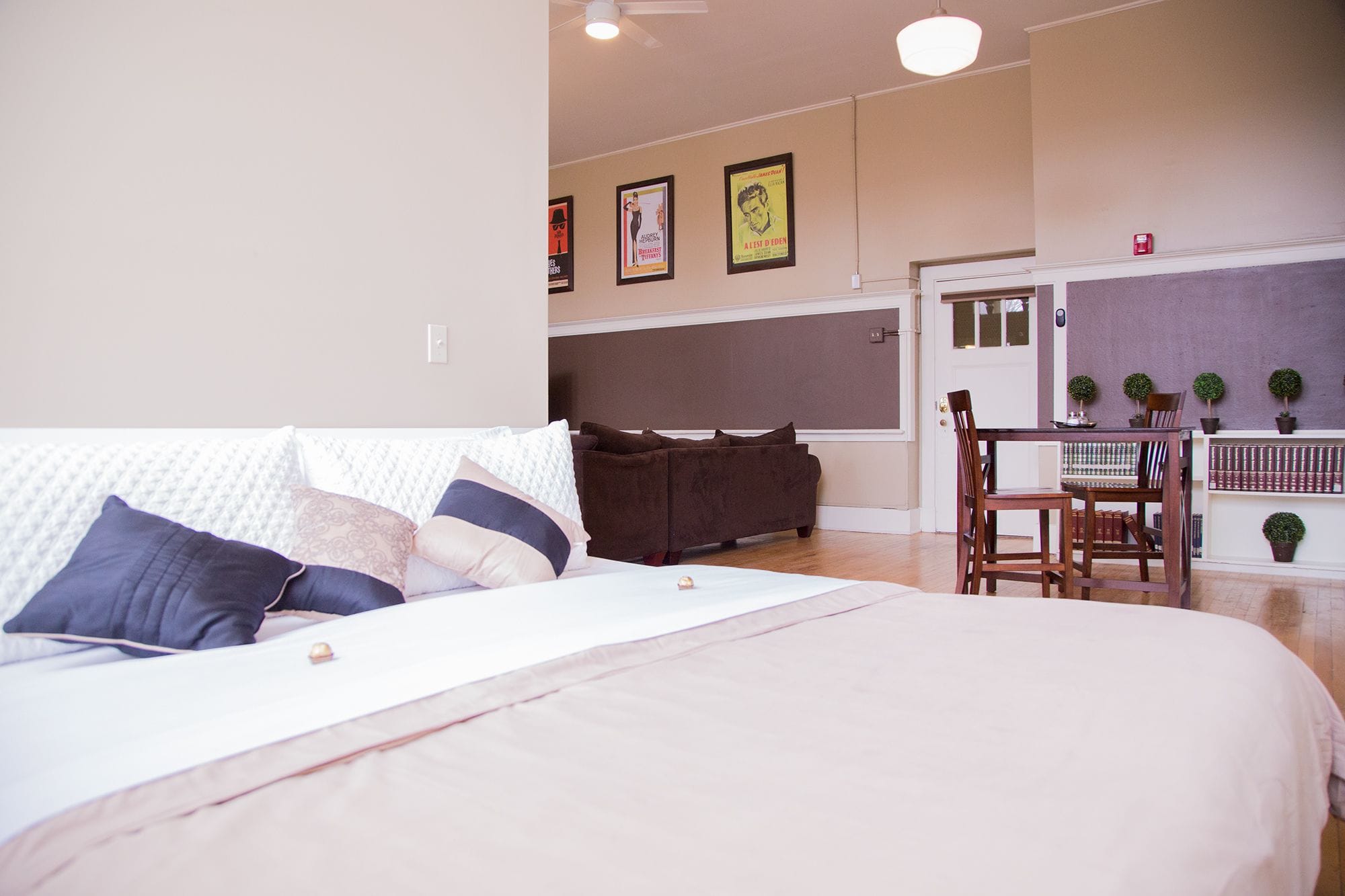 A bedroom with a bed, a sofa, a dining table with chairs, and a small kitchen area.