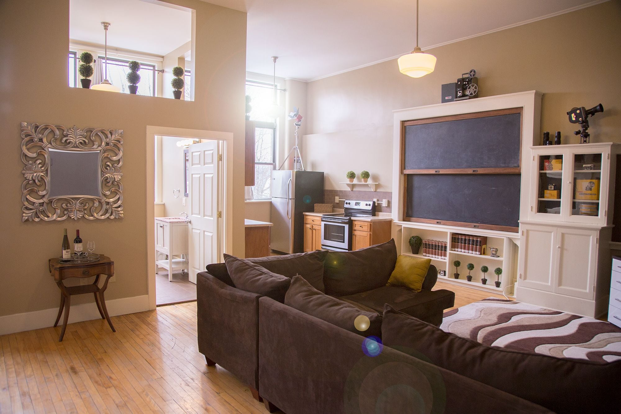 A living room with a sofa, a dining area with a table and chairs, a kitchen with appliances, and a large window.