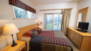 A bedroom with a bed, a nightstand, a lamp, a dresser, a television, and a window with curtains.
