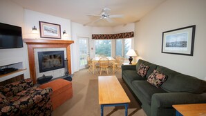 A living room with a fireplace, a television mounted on the wall, a dining table with chairs, a sofa, and a coffee table.
