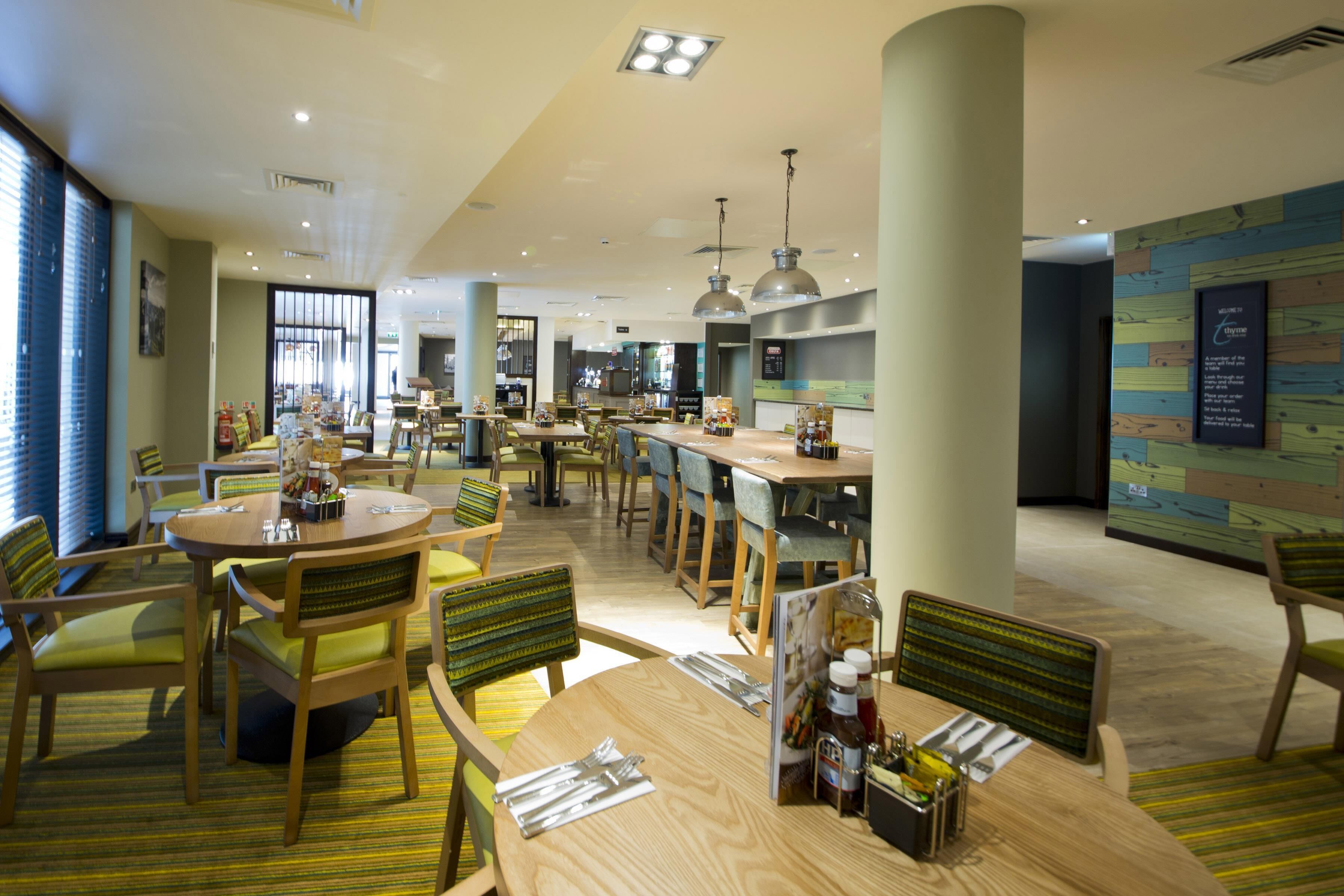 A spacious hotel dining area with multiple tables and chairs, a central island, and a view of the kitchen in the background.