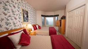 Une chambre avec deux lits, un papier peint à motifs floraux, une fenêtre donnant sur un beau paysage et une armoire.