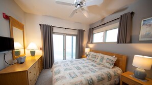 A hotel room with a bed, bedside lamps, a ceiling fan, a TV, a wooden dresser, and a window with curtains. - Mountainside Suite! Arcade, Pool, Hot Tub Access (Ludlow)