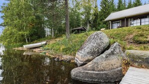 Un chalet au bord du lac, doté d’un quai, entouré d’une forêt dense et avec un petit bateau à proximité.