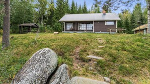 Une cabane dotée d’un grand porche, entourée d’une pelouse et de gros rochers.