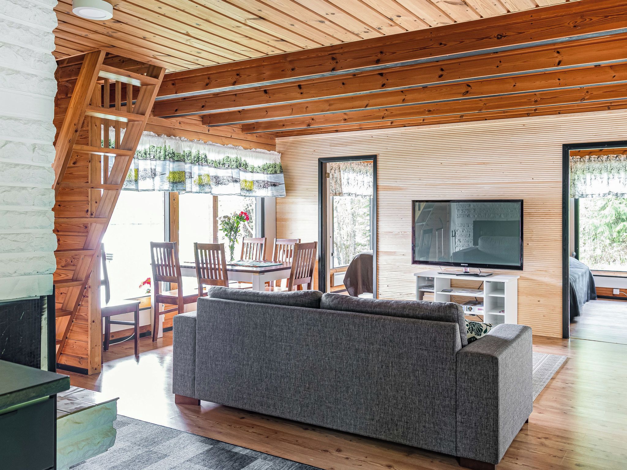 Ein modernes Wohnzimmer mit Sofa, Fernseher und Holzbalkendecke.