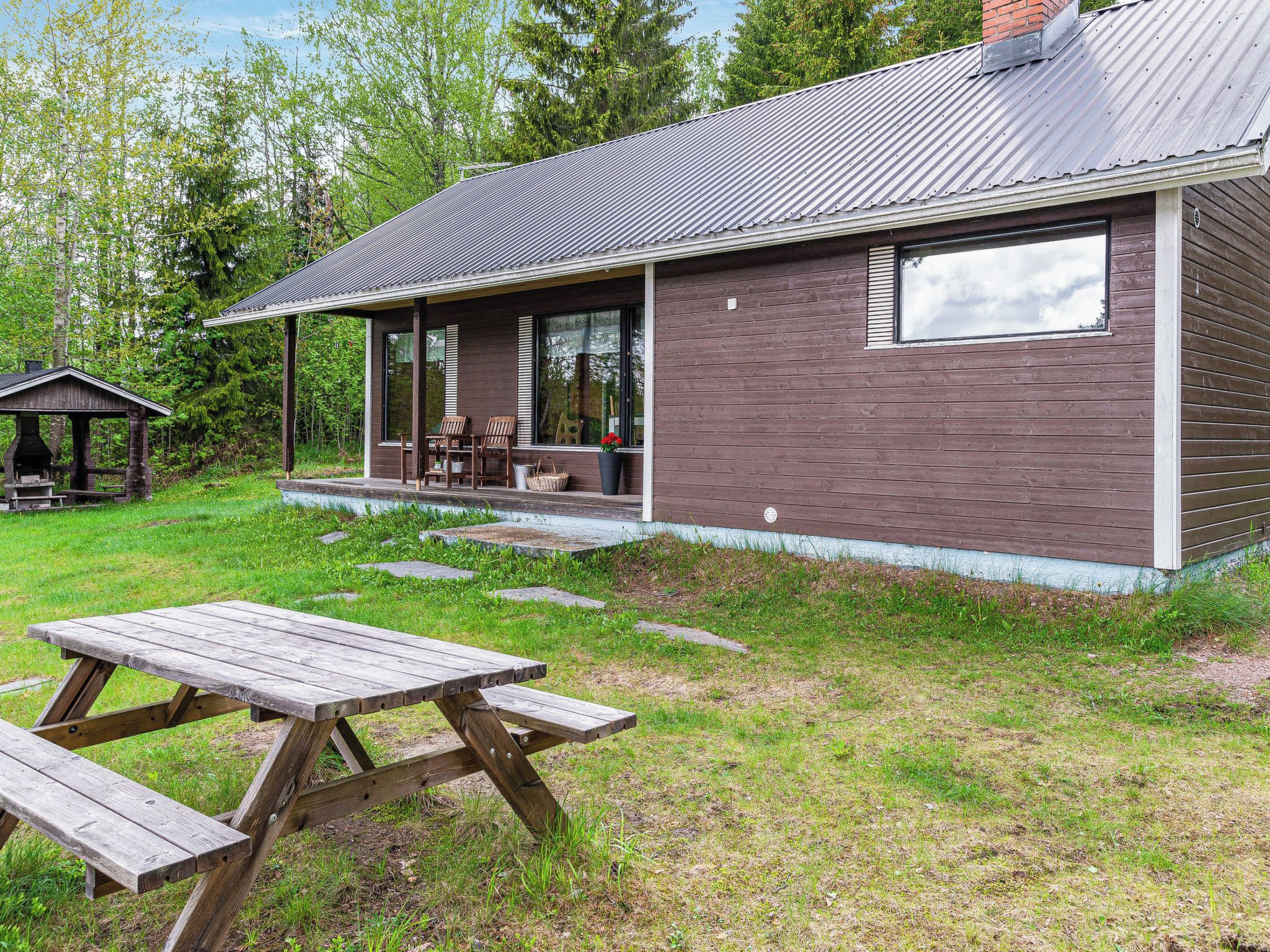 Ein rustikales Blockhaus mit überdachter Veranda, einem Picknicktisch und einem kleinen Grill.