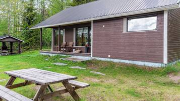 En enkel stuga med en veranda, ett picknickbord och en liten utegrill.