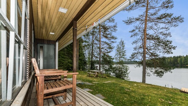 Une terrasse en bois avec un banc, donnant sur un lac bordé d’arbres et sous un ciel dégagé.
