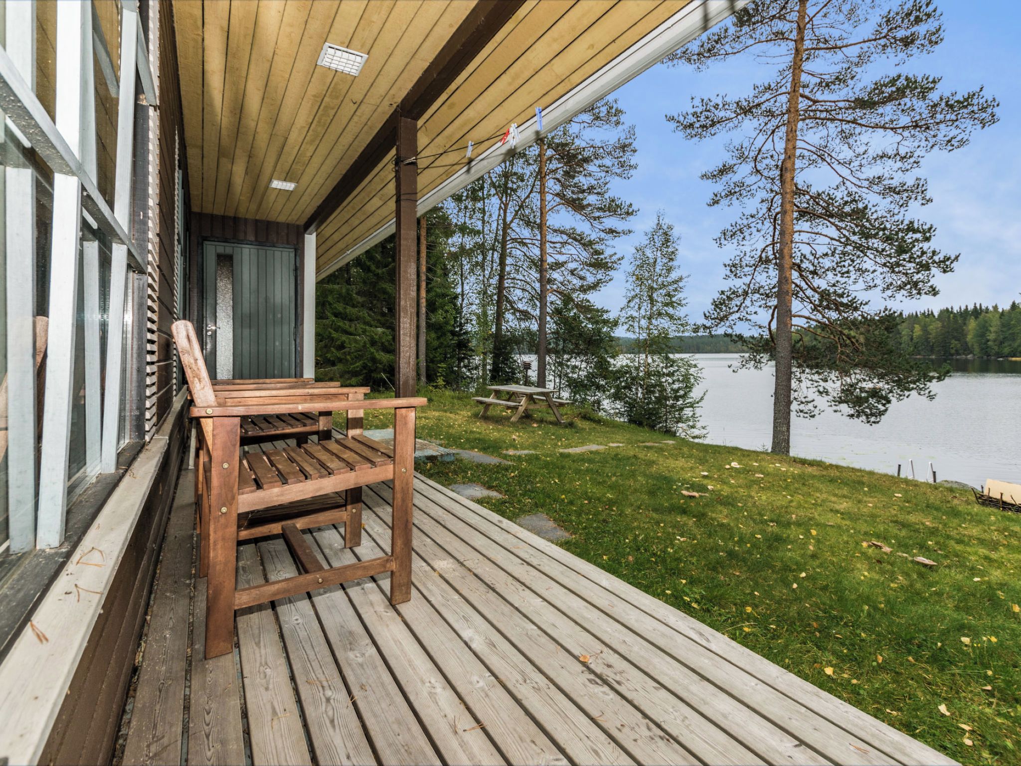 Een houten terras met een bank en tafel, met uitzicht op een meer met bomen.