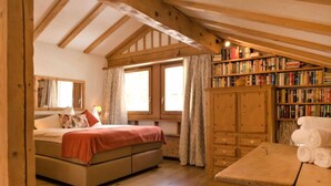 A cozy room with a bed, a wooden table with towels, a bookshelf, and a window with curtains.