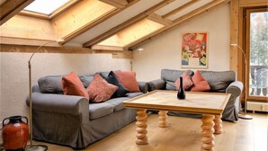 A cozy room with a sloped ceiling, wooden beams, a grey sofa with cushions, a wooden coffee table, and a vase.