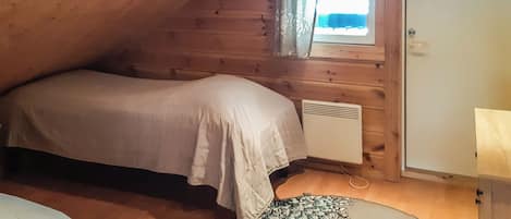 A small, cozy room with a sloped ceiling, a single bed, a radiator, and a window with curtains.
