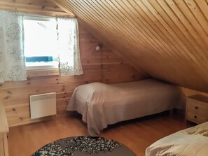 Un dormitorio acogedor en el ático, con techo inclinado, una cama individual, un radiador y una ventana con cortinas.