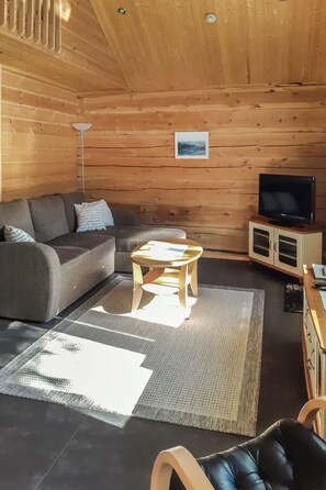 Interior acogedor de una cabaña con sofá, una mesita, televisor en mueble bajo y un cuadro en la pared.