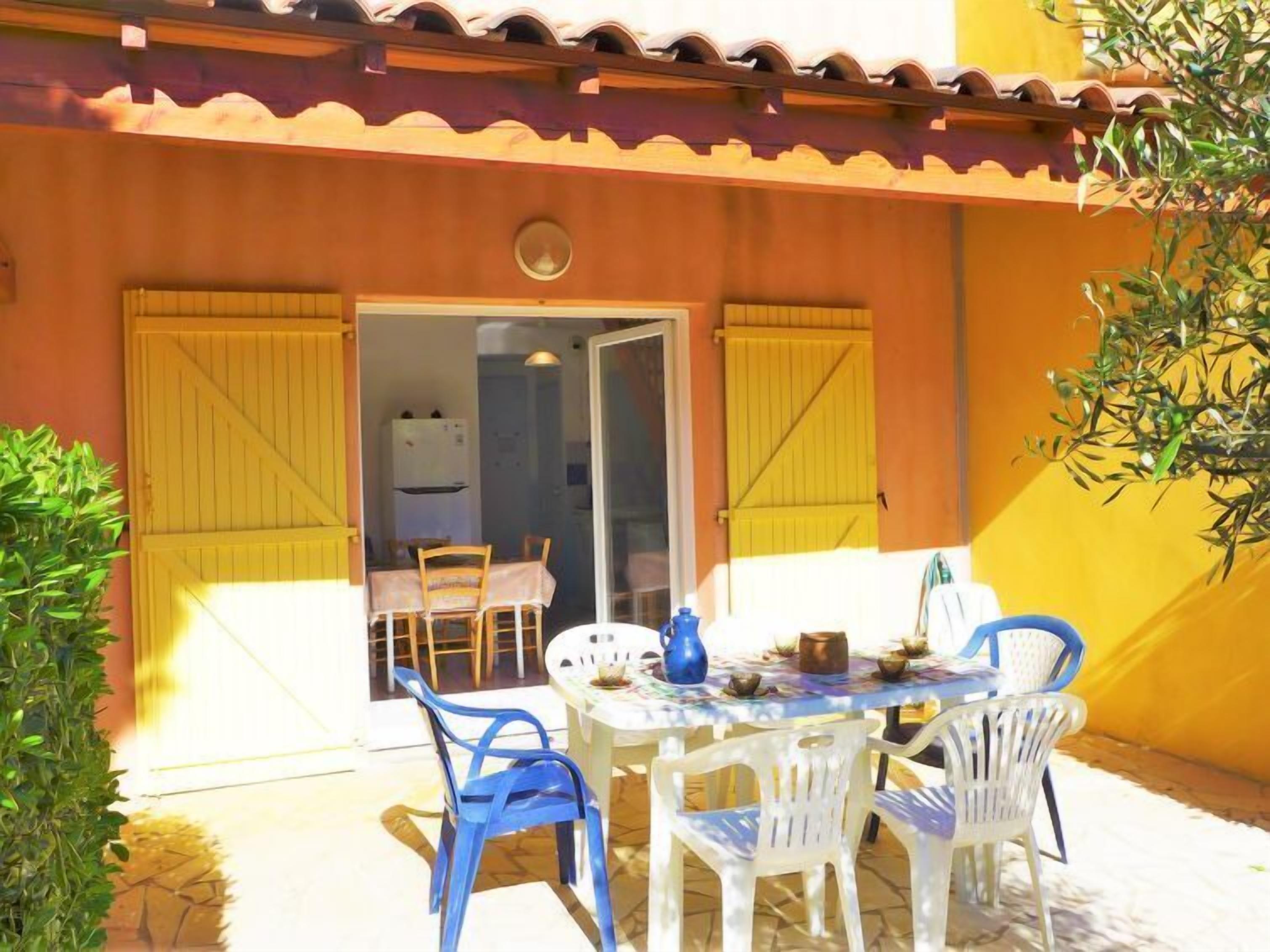 Eine Terrasse im Freien mit Tisch und Stühlen, einer Tür, die zu einem Zimmer führt, und einer gelben Wand.
