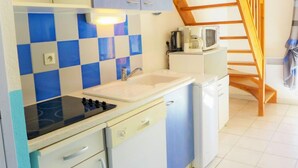 A compact kitchen with a sink, stove, and microwave. There is a wooden staircase leading to another level. - Plein Sud by Interhome (Narbonne-Plage)