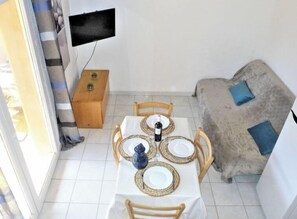 A dining area with a table set for four, a television mounted on the wall, and a sofa with cushions.