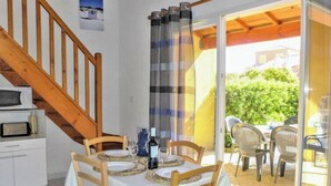 A dining area with a table set for four, wooden chairs, a bottle of wine, and a glass. A staircase leads to an upper level. - Plein Sud by Interhome (Narbonne-Plage)