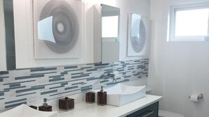 Ein modernes Badezimmer mit einem weißen Waschbecken, dunklen Schränken, einem gemusterten Hocker und einer Toilette.
