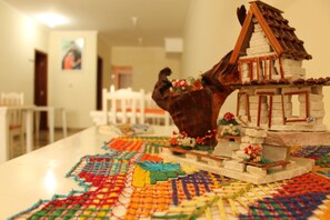 A table with a colorful woven mat, a wooden horse sculpture, and a small house model. - Pousada Saint Alban (Cachoeira Paulista)