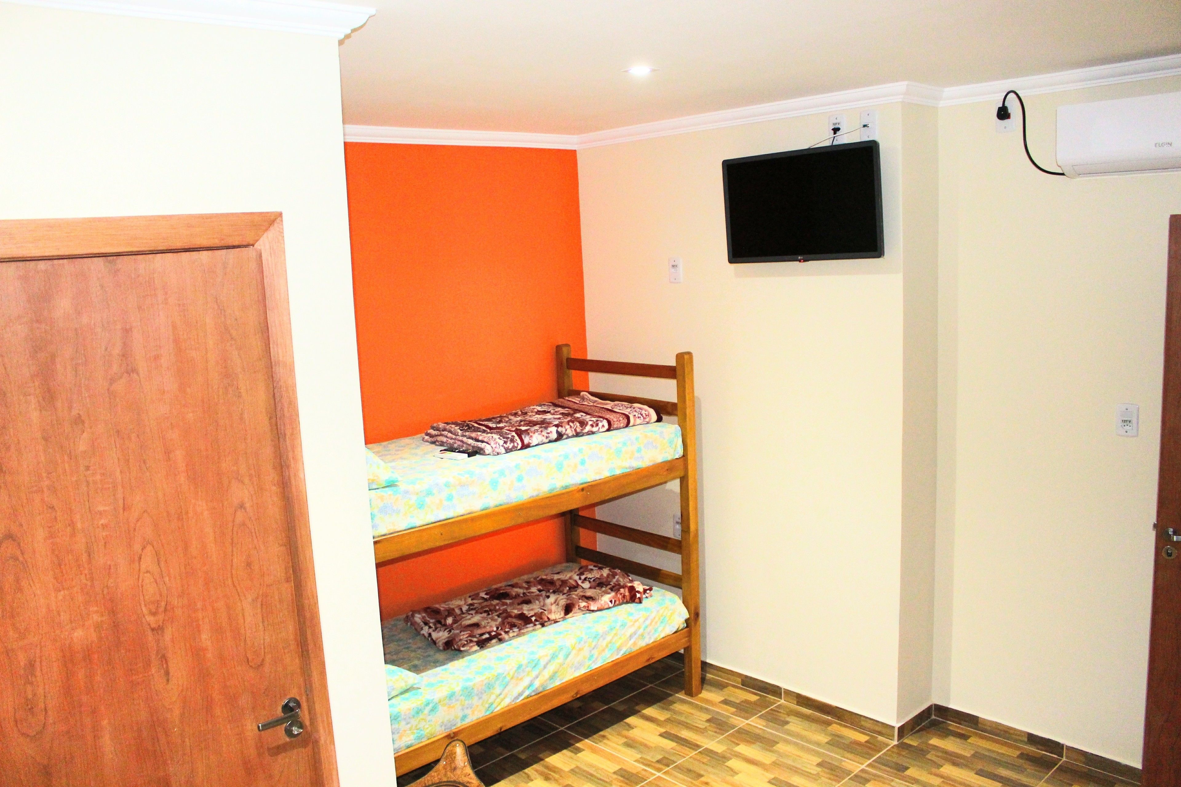 A room with a bunk bed, a television mounted on the wall, and an air conditioning unit.