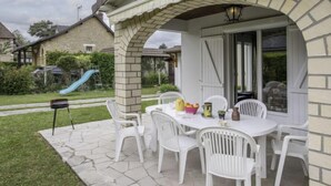 An outdoor patio area with a stone-tiled floor, white plastic chairs, and a table set for dining. - Villa Hélios by Interhome (Cabourg)