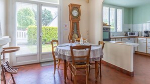 A dining area with a round table, chairs, a clock, and a kitchen with a microwave. - Villa Hélios by Interhome (Cabourg)