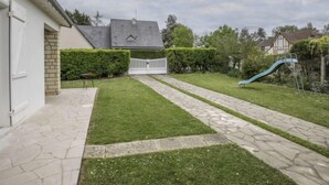A residential backyard with a paved pathway, a small lawn, a white gate, and a blue slide. - Villa Hélios by Interhome (Cabourg)