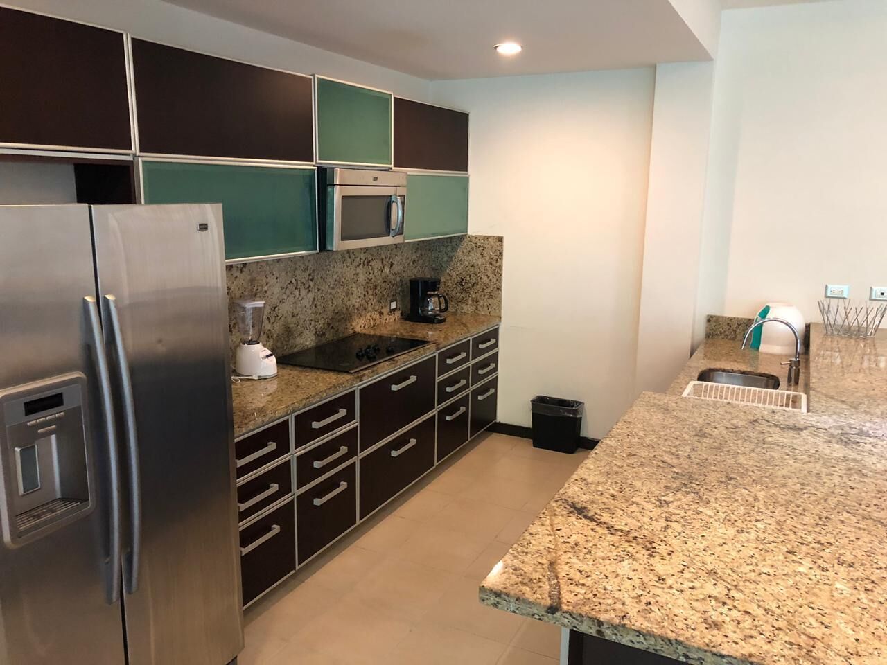 A modern kitchen with a granite countertop, stainless steel appliances, and dark cabinetry.