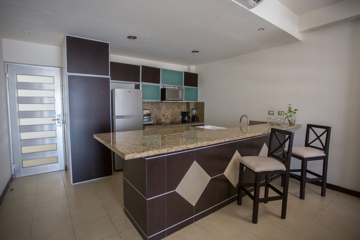 A modern kitchen with a central island, dark cabinetry, and a tiled backsplash.