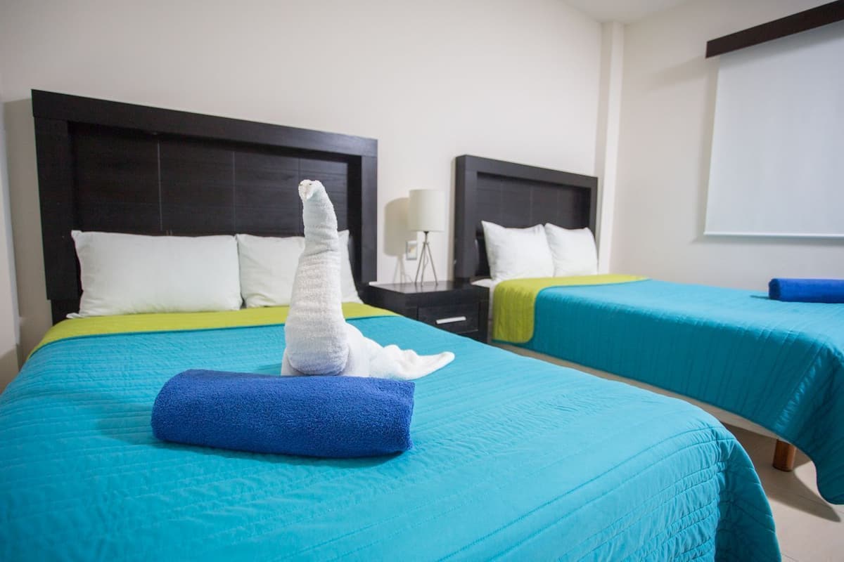 Ein Hotelzimmer mit zwei Betten, jeweils mit blauer Bettdecke und weißen Kissen.