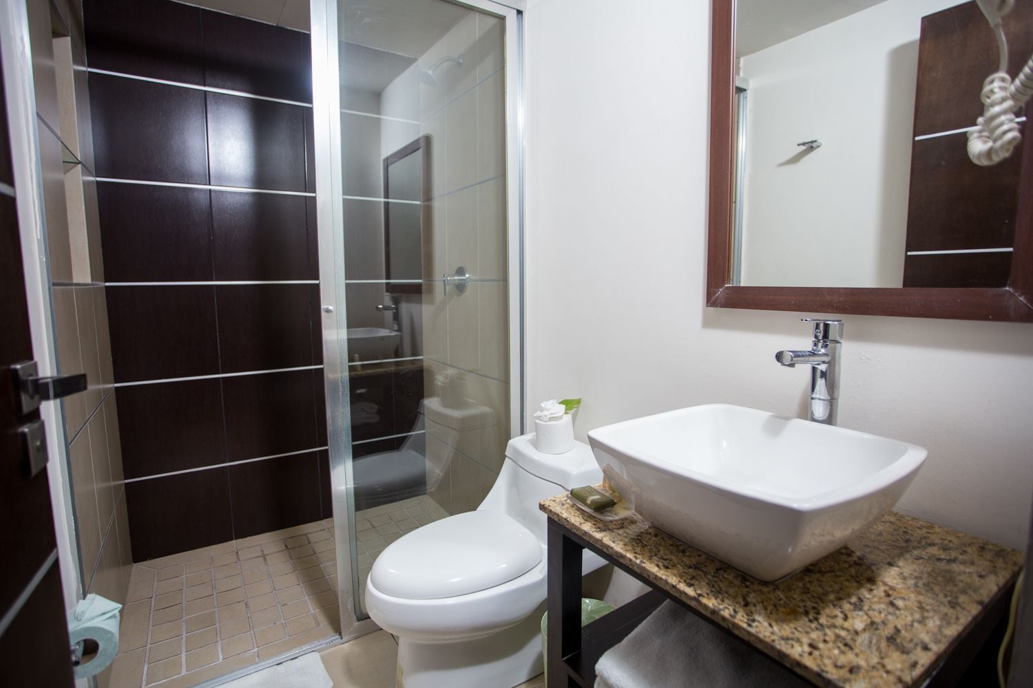 A bathroom with a glass shower enclosure, a white toilet, a sink with a granite countertop, and a mirror above the sink.