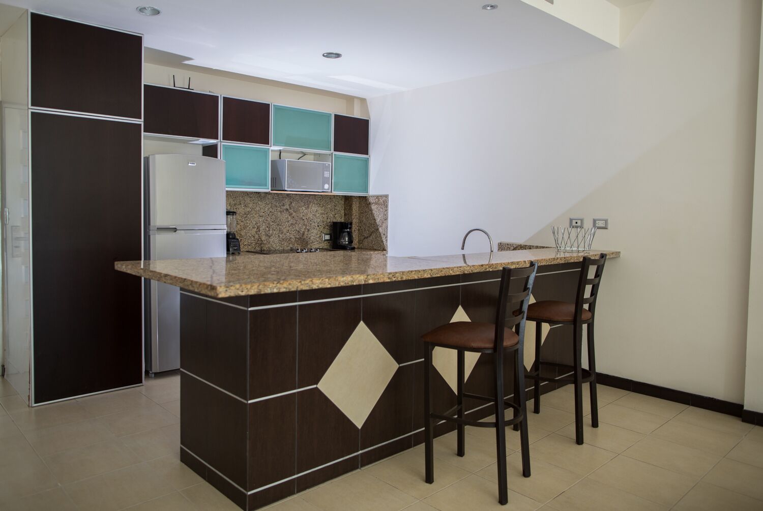 A modern kitchen with a granite countertop, dark cabinetry, and a built-in island with bar stools.