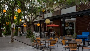 An outdoor cafe area with tables and chairs, surrounded by trees and a building with a modern design. - San Pedro Hotel 5ta Avenida (Playa del Carmen)