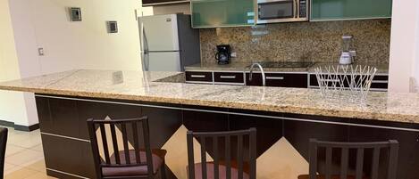 A modern kitchen with a granite countertop, stainless steel appliances, and three bar stools.