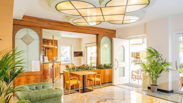 Un hall d’entrée spacieux avec un sol en marbre, un canapé vert et un comptoir d’accueil en bois.