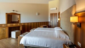 Une chambre d’hôtel avec un grand lit, un bureau en bois, un miroir et une lampe de chevet.