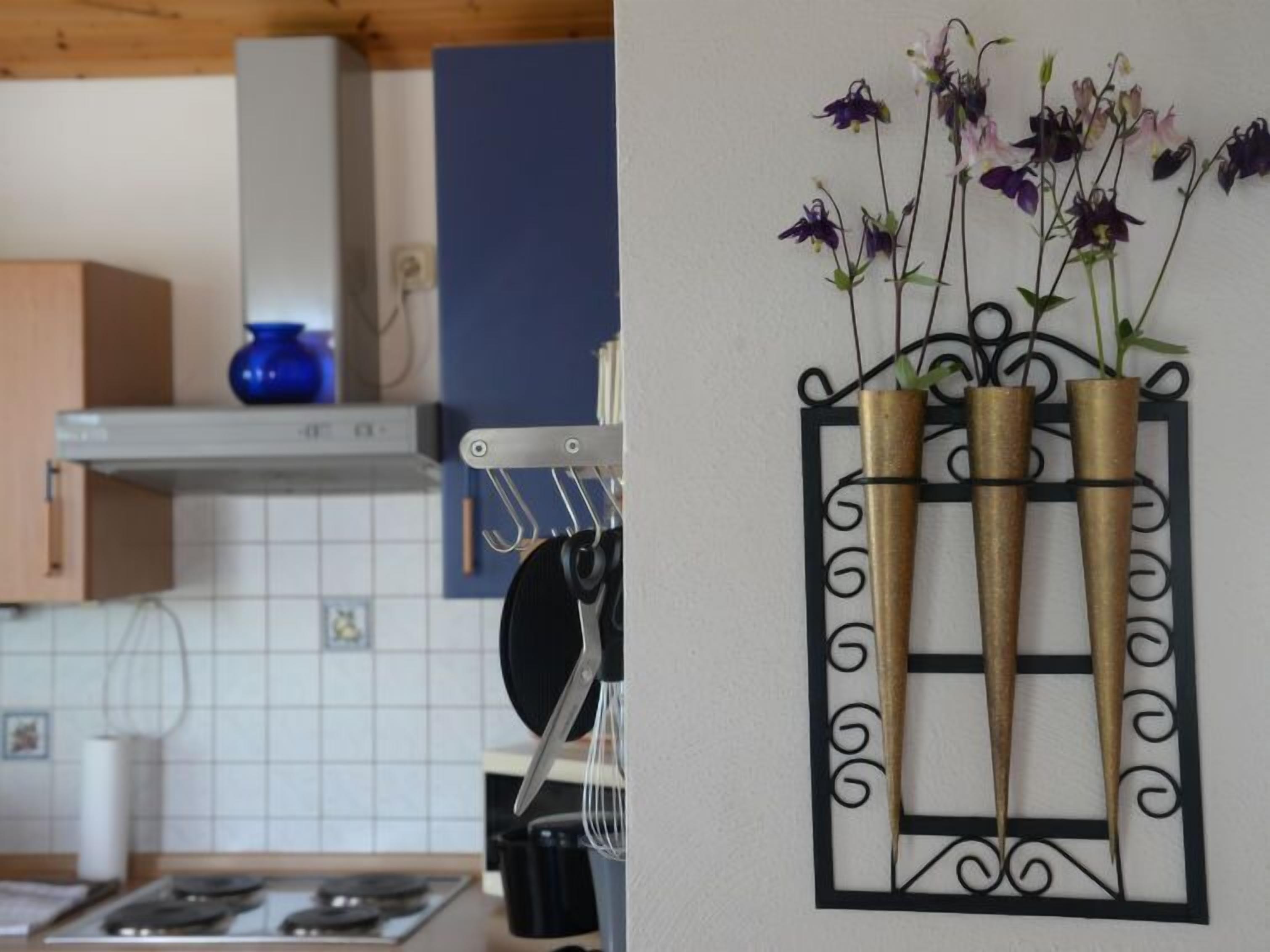 A kitchen with a stove, a blue vase on the shelf, and a wall-mounted metal rack holding three bamboo vases with flowers.