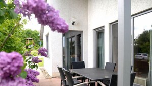 An outdoor patio with a table and chairs, surrounded by large windows and a view of a garden. - Solling by Interhome (Uslar)