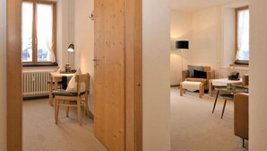 Una habitación moderna y bien iluminada con una puerta de madera, un escritorio con silla, un sofá y una lámpara.