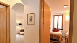 Habitación de hotel con puerta de madera, cama con almohada roja, mesita de noche y ventana con cortinas.